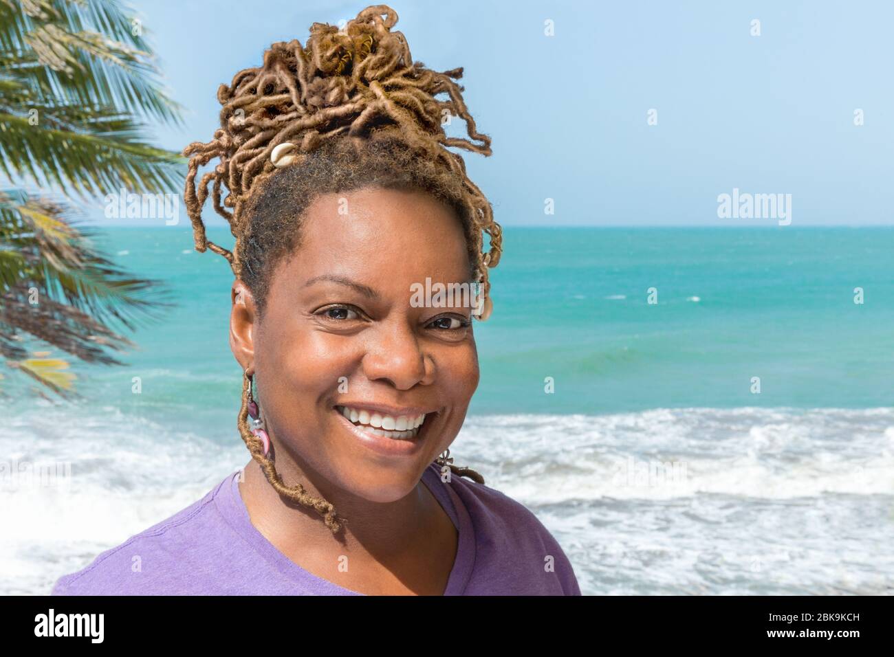 Close Up Ritratto di bella donna nera, africana, o carribea ridendo all'aperto che si affaccia sulla splendida spiaggia e l'oceano. Foto Stock