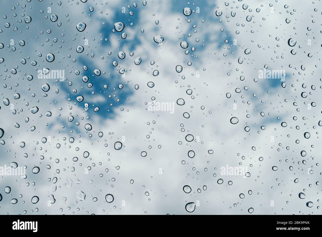 Acqua fresca gocce di rugiada su vetro trasparente con sfocatura nuvolosa sfondo del cielo Foto Stock