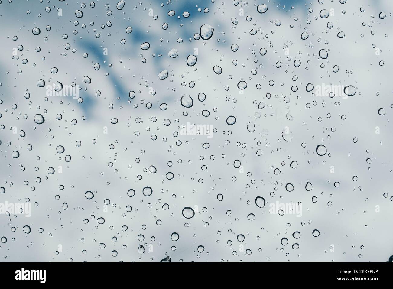 Acqua fresca gocce di rugiada su vetro trasparente con sfocatura nuvolosa sfondo del cielo Foto Stock