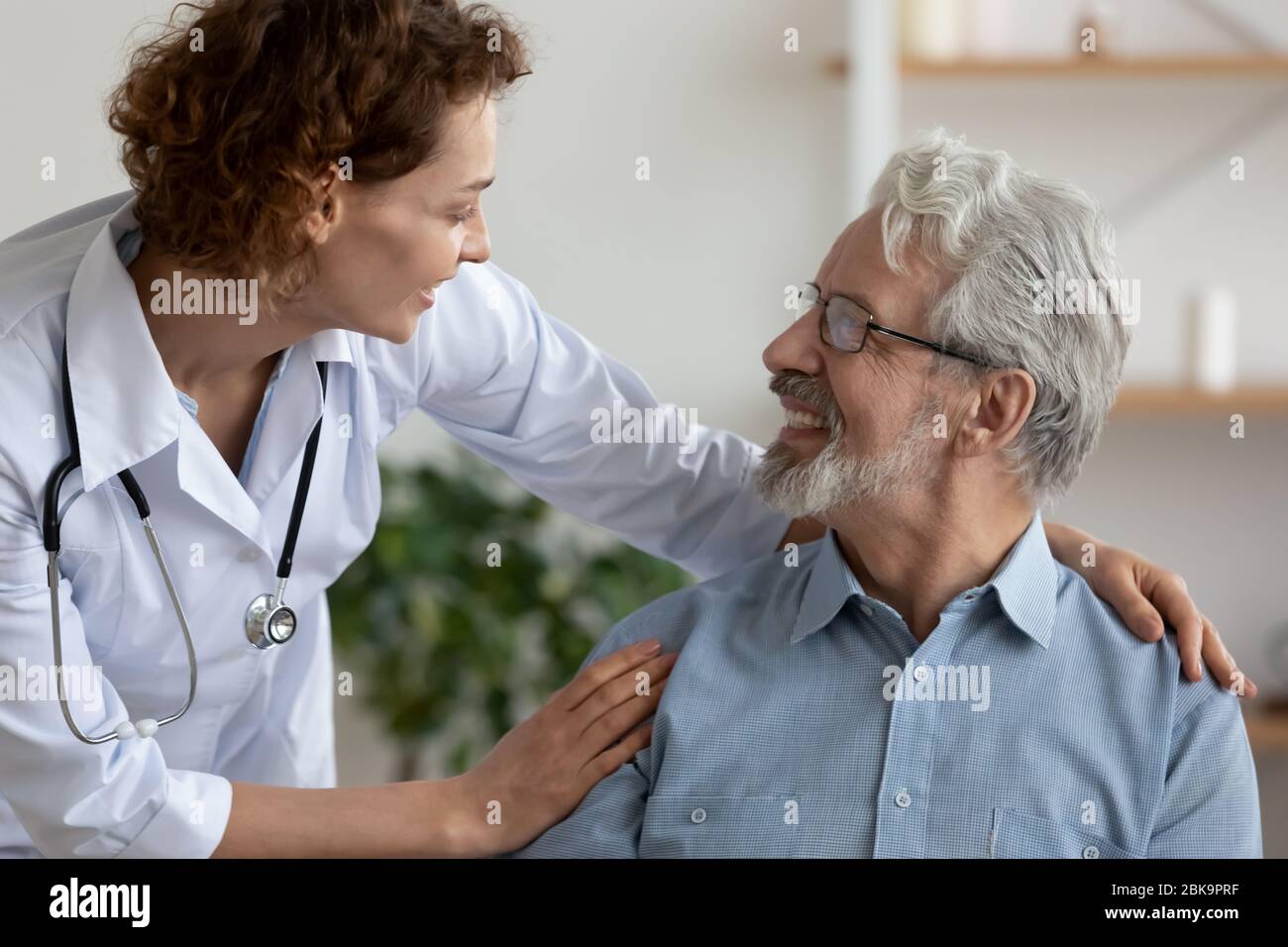 Medico curante femminile che abbraccia aiutando il paziente maschio anziano felice Foto Stock
