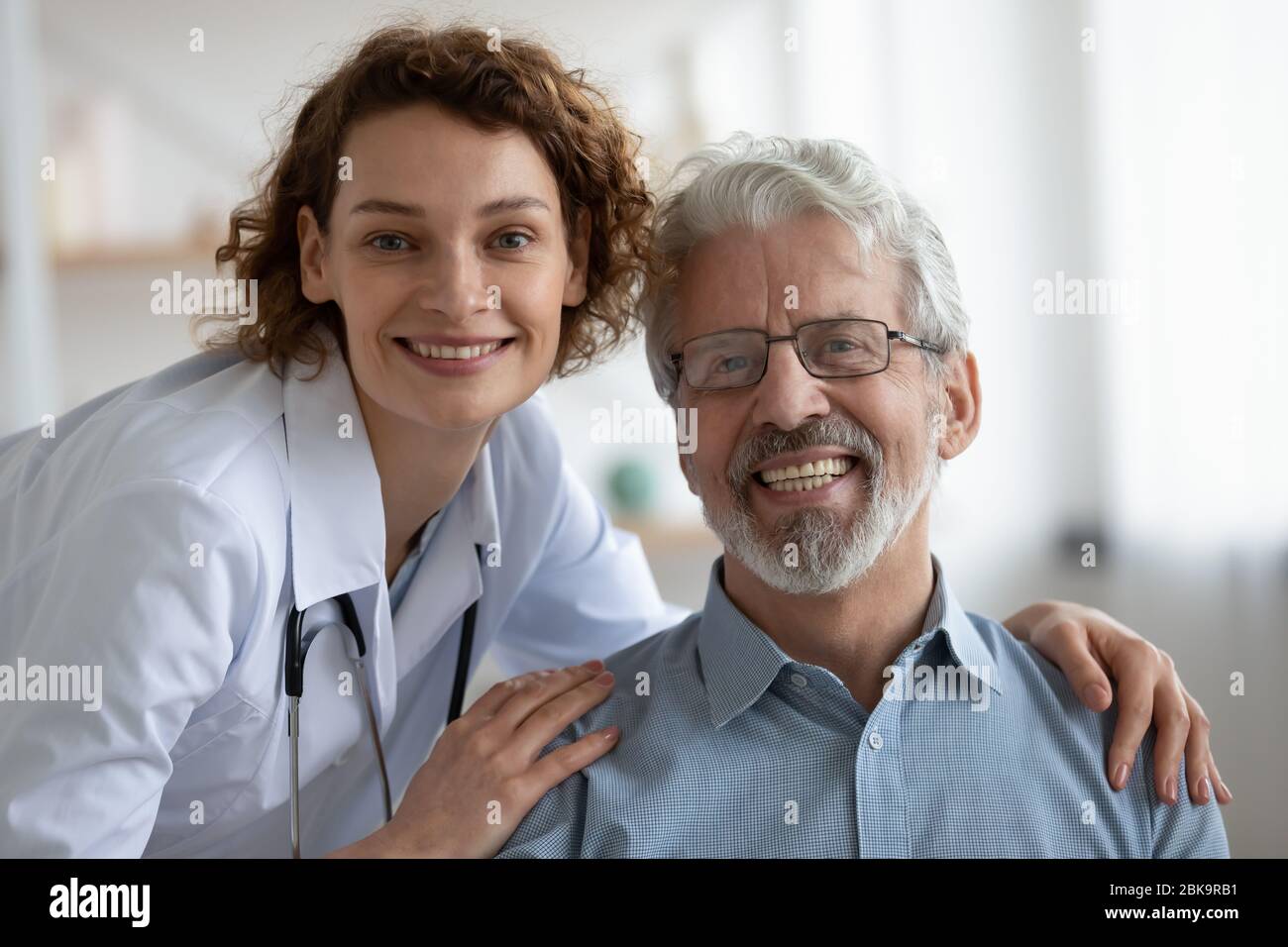 Giovane giovane donna giovane e felice medico che abbraccia il paziente maschile senior, ritratto Foto Stock