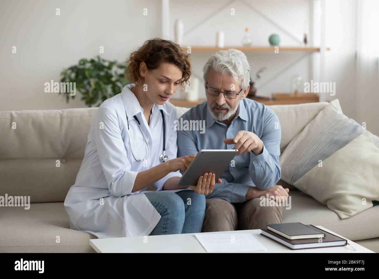 Medico femminile che utilizza un tablet digitale per consultare il paziente senior a casa Foto Stock