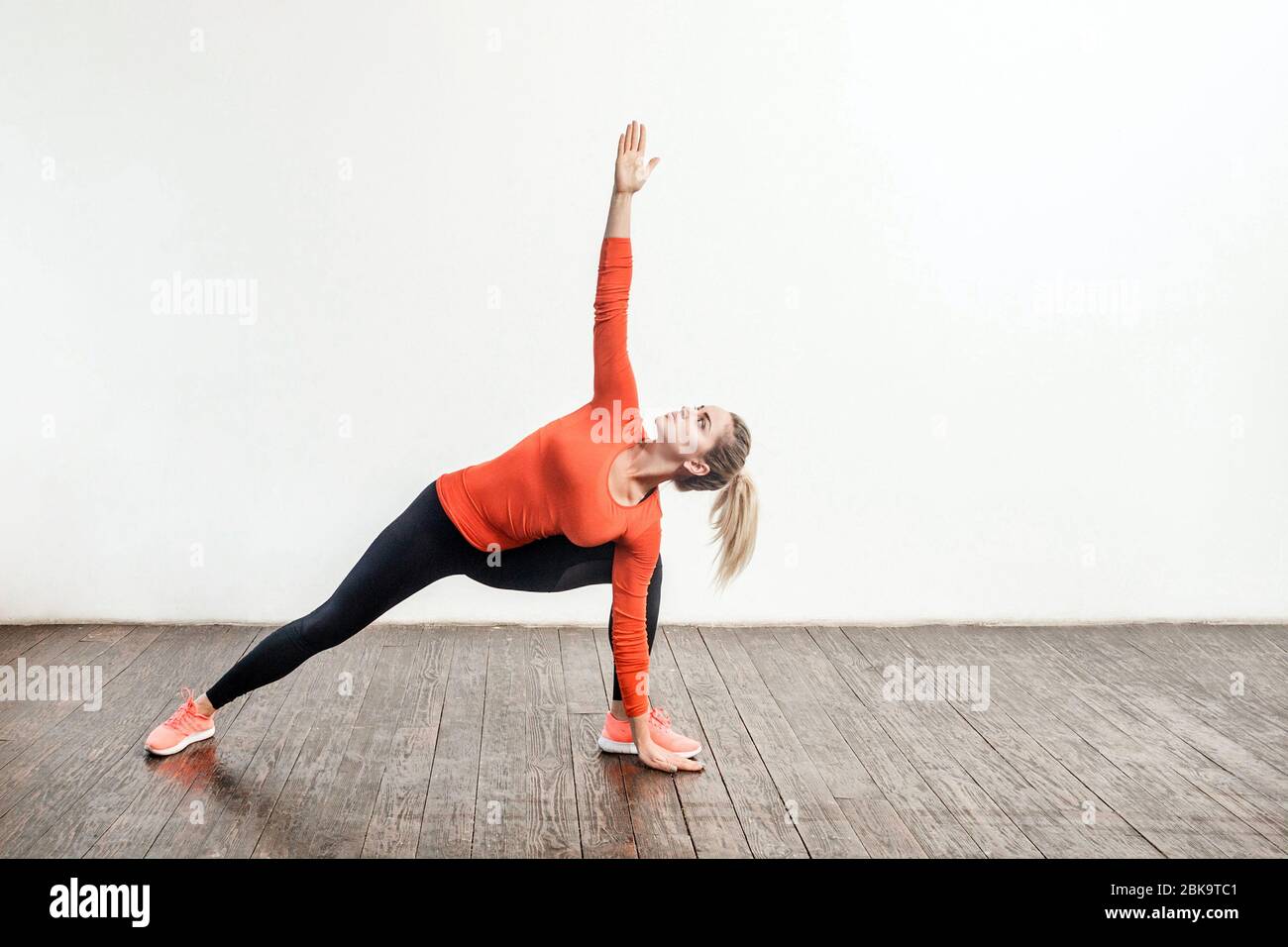Donna bionda sottile in stretto abbigliamento sportivo pratica yoga, in piedi in trikonasana posa triangolare, allenare i muscoli per la flessibilità. Assistenza sanitaria, sport atto Foto Stock