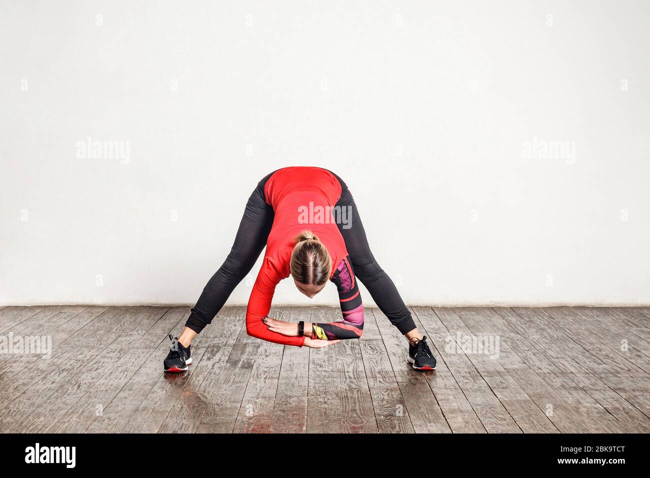 Atletica giovane donna sottile in stretto abbigliamento sportivo piegandosi verso il basso, allungando i muscoli per la flessibilità, riscaldamento prima di allenarsi in palestra a casa. Salute Foto Stock