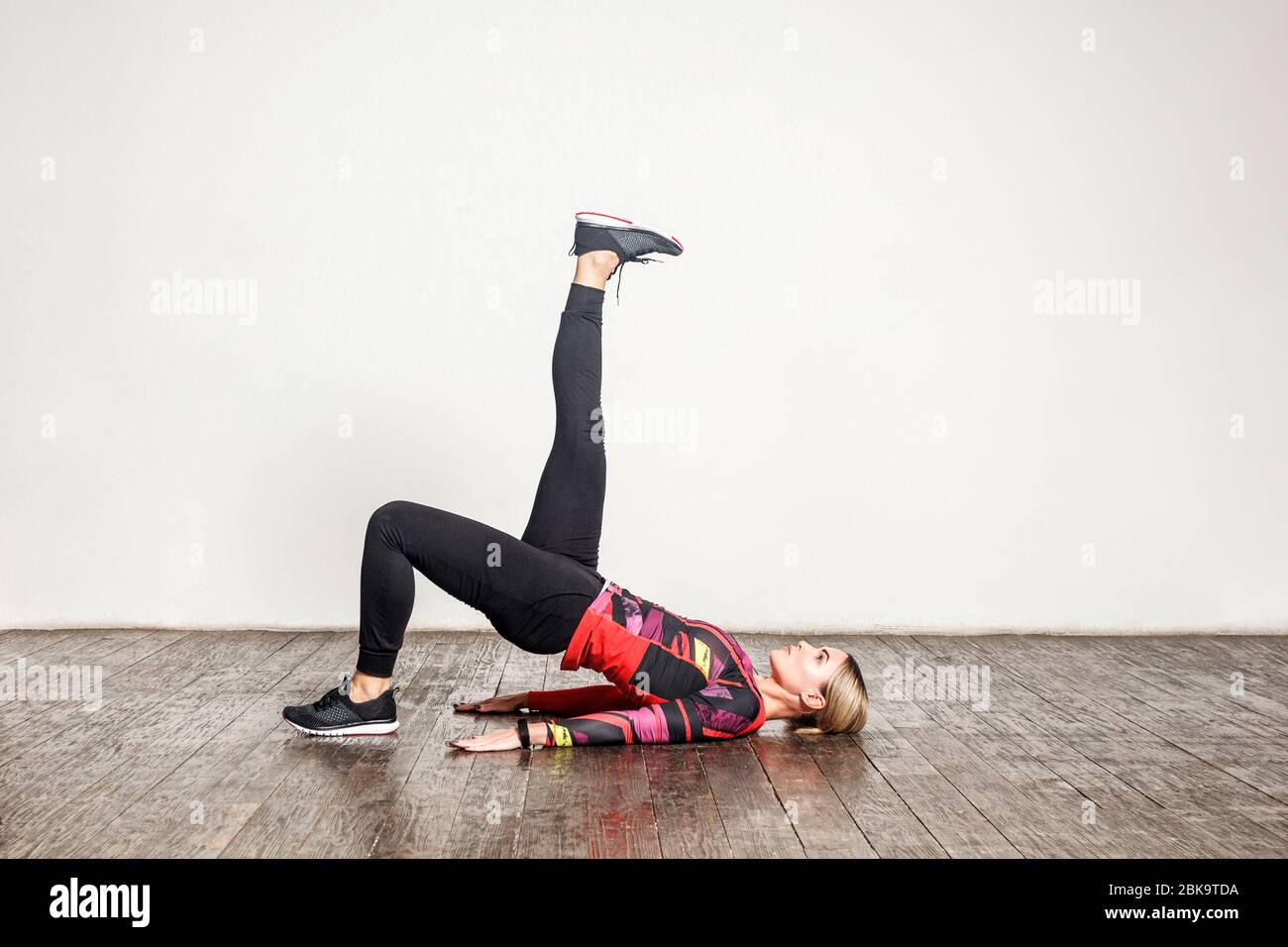Giovane donna sottile in stretto abbigliamento sportivo pratica yoga, facendo una posa ponte gambe con sollevamento gamba, flessibilità di allenamento, forza muscolare. Assistenza sanitaria Foto Stock