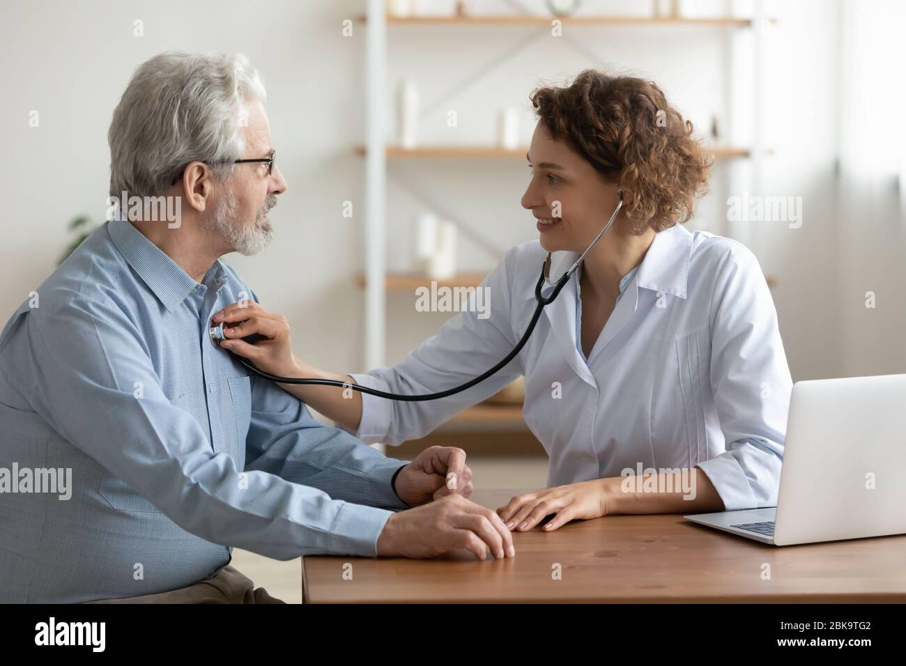 Medico femminile che ascolta il cuore del paziente maschio anziano usando lo stetoscopio Foto Stock
