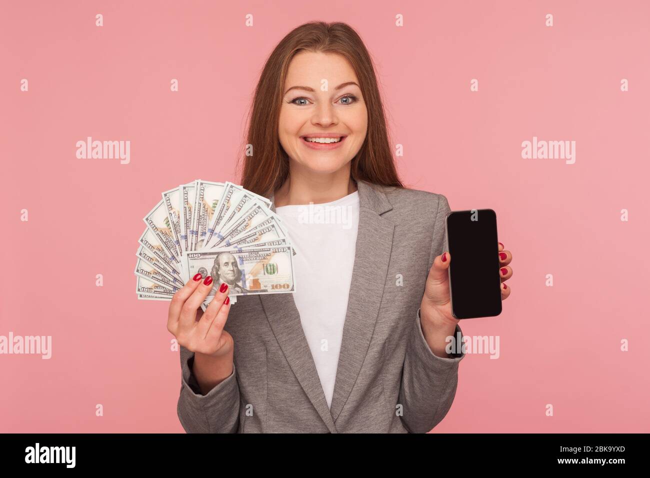 Domanda online, domanda di prestito. Ritratto di felice donna d'affari sorridente in giacca vestito con banconote dollaro e cellulare, soddisfatto con mobile b Foto Stock