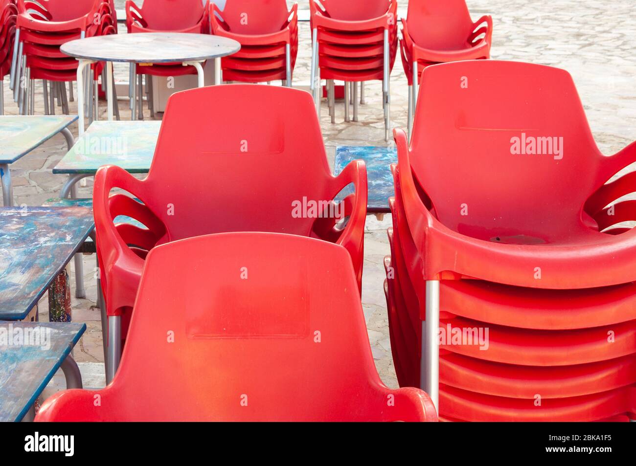 Sedie rosse di plastica accatastate accanto ai tavoli da esterno. Le  aziende di ristoranti sono chiuse da Coronavirus Foto stock - Alamy