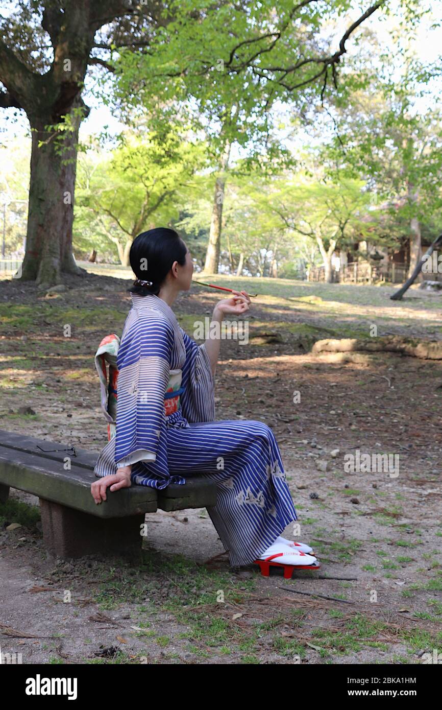 Donna giapponese in kimono fumante tradizionale pipa da fumo (kiseru) su una panca in un parco Foto Stock