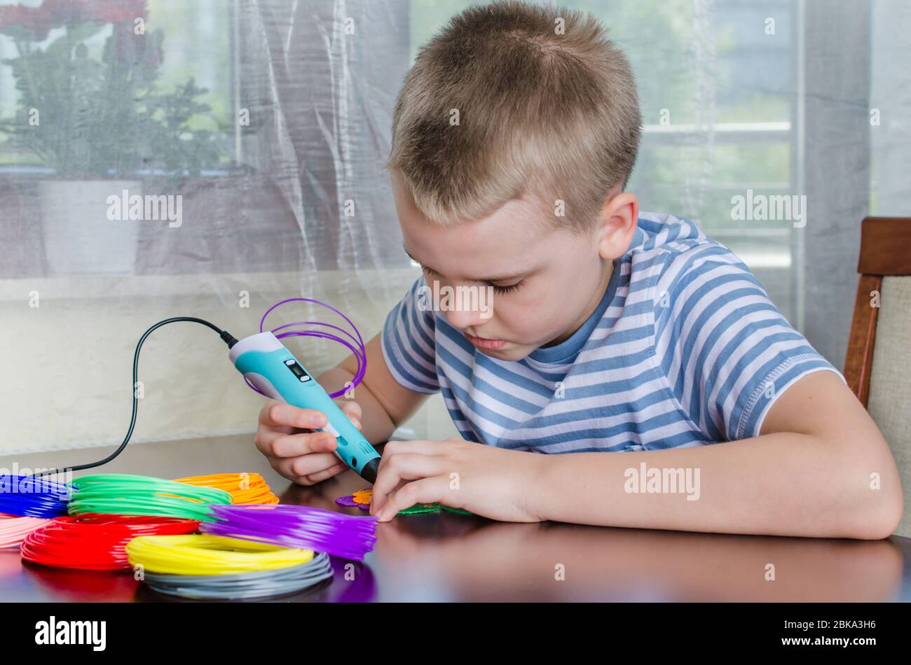 Ragazzo con penna 3D. Felice bambino che fa il fiore dalla plastica ABS colorata. Hobby creativo a casa, tecnologia, tempo libero, concetto di istruzione. Foto Stock