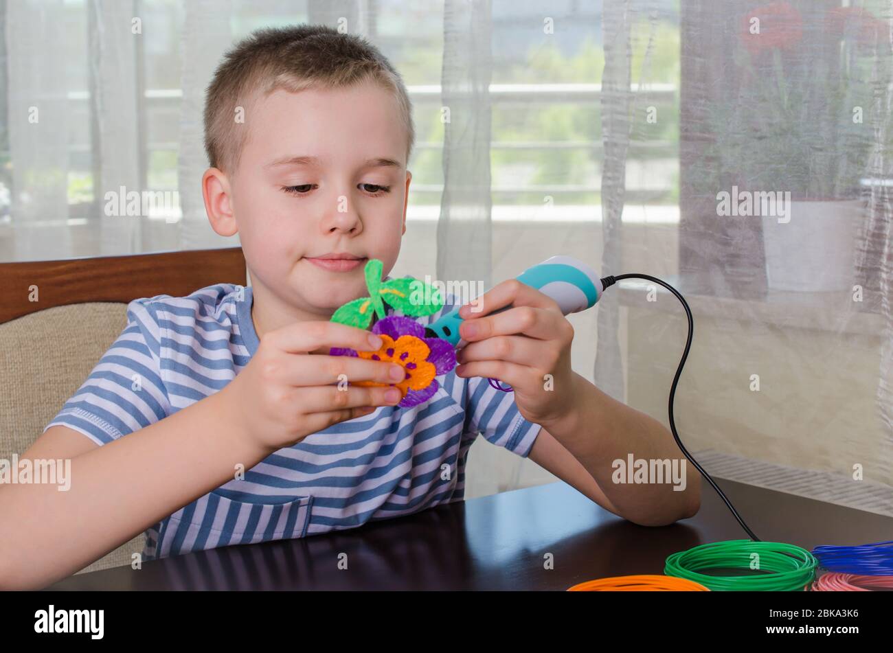 Ragazzo con penna 3D. Felice bambino che fa il fiore dalla plastica ABS colorata. Hobby creativo a casa, tecnologia, tempo libero, concetto di istruzione. Foto Stock