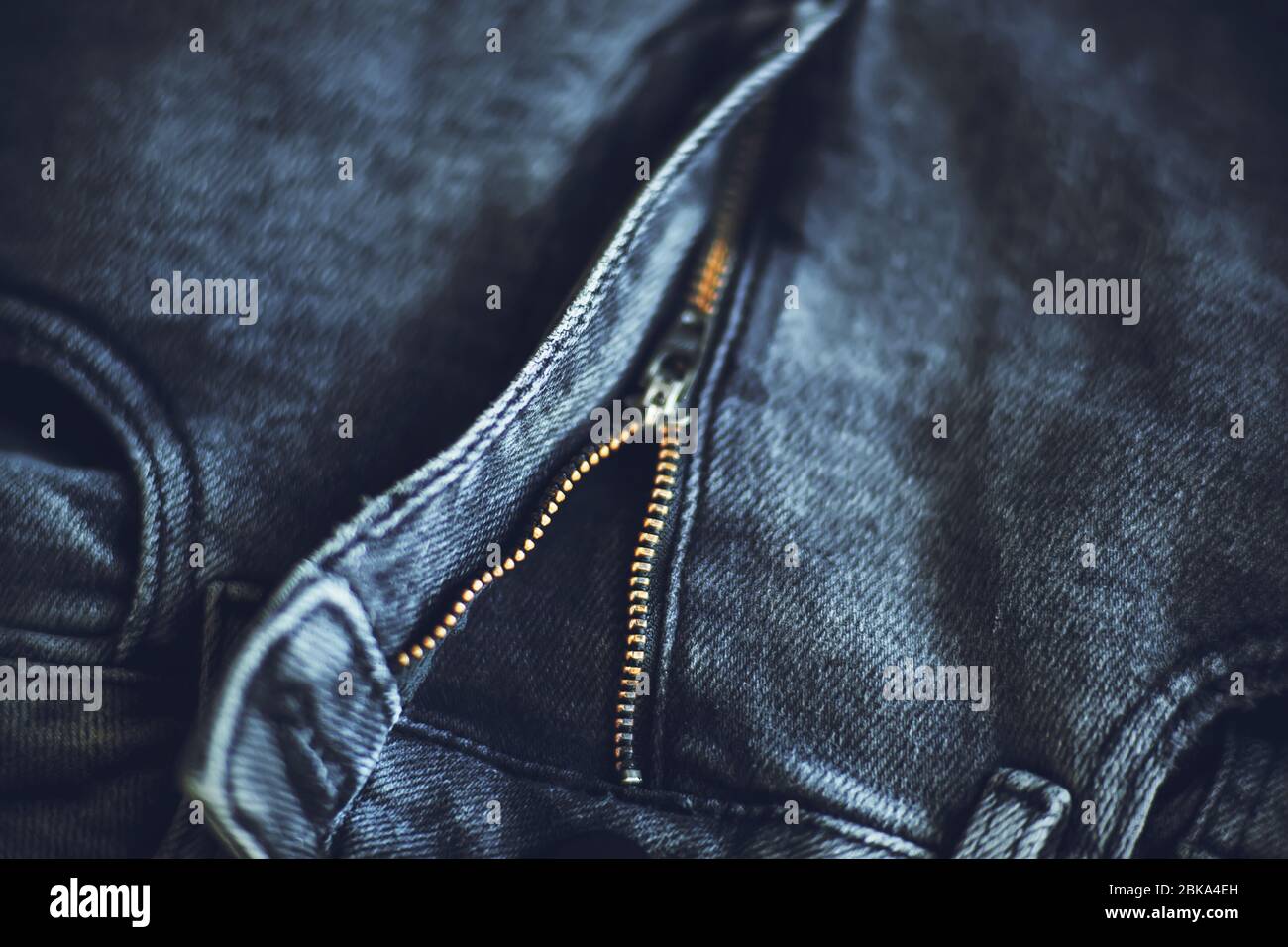 La parte superiore dei jeans alla moda grigio scuro in tessuto grezzo, che si fissa con una zip, illuminata dalla luce. Foto Stock