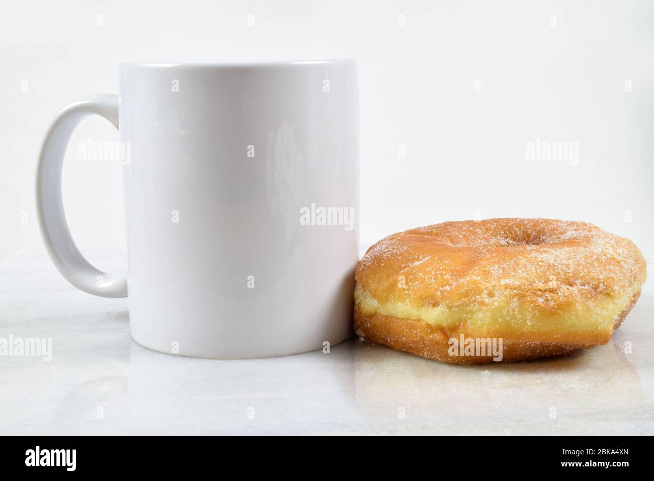 Una deliziosa ciambella rivestita di zucchero si trova tentevolmente accanto a una tazza da caffè da 11 ml. Foto Stock
