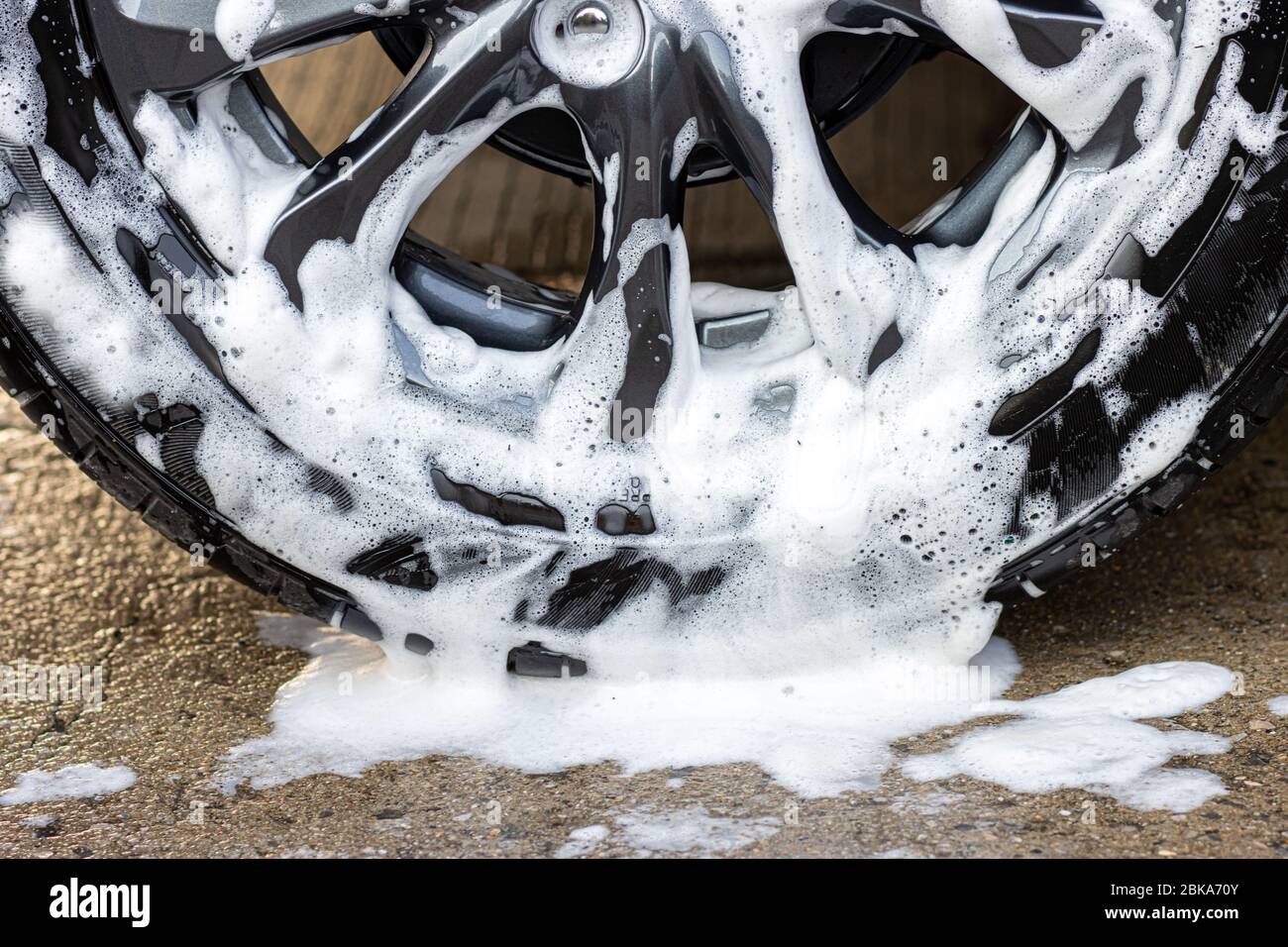 Una parte di ruota di auto con flusso in schiuma bianca. Acqua saponata al volante della lavatrice, vista ravvicinata. Foto Stock