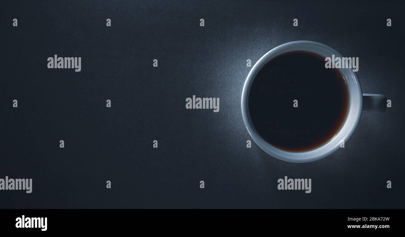 Flatlay, vista dall'alto di scuro e di moody illuminato una tazza da caffè con sfondo nero e duro scarsa luce spazio di copia contidion Foto Stock