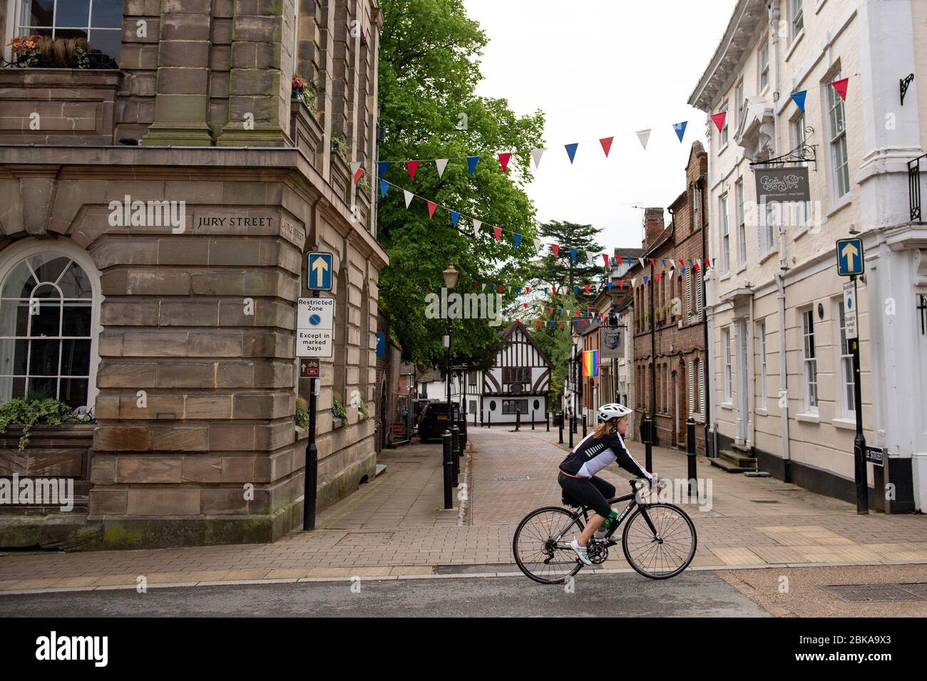 Un ciclista che corre lungo una tranquilla Warwick High Street, Warwick come la maggior parte delle città vede meno visitatori, mentre il Regno Unito continua a fare un giro a chiave per contribuire a frenare la diffusione del coronavirus. Foto Stock