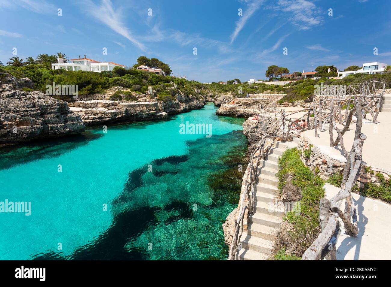 Acqua turchese, terrazze e scale a Cala en Brut, un popolare luogo di nuoto vicino a Cala en Blanes, Minorca, Spagna Foto Stock
