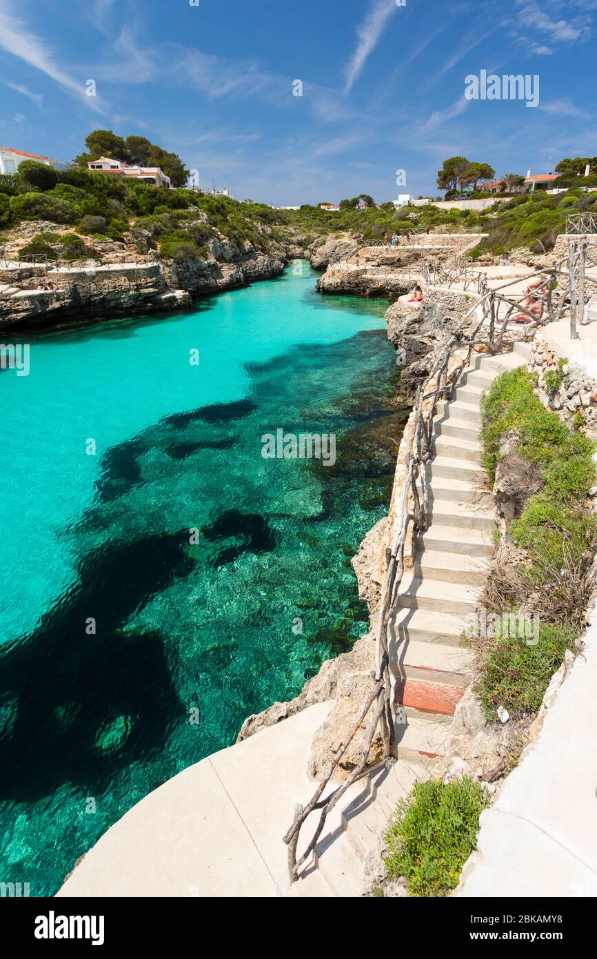 Acqua turchese, terrazze e scale a Cala en Brut, un popolare luogo di nuoto vicino a Cala en Blanes, Minorca, Spagna Foto Stock