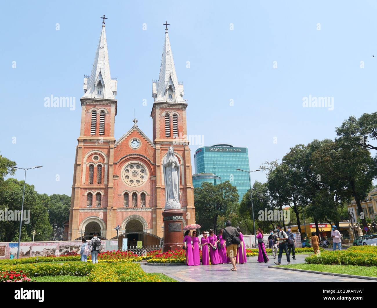 Ho Chi Minh City, Vietnam - 30 aprile 2020: Un grande gruppo di Signore in magenta brillante tradizionale vietnamita lungo vestito di fronte alla Notre-Dame Cathe Foto Stock
