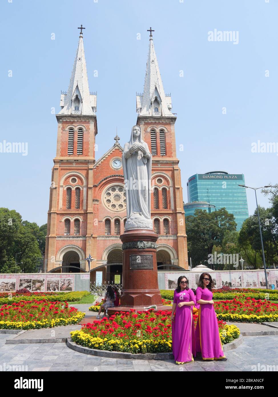Ho Chi Minh City, Vietnam - 30 aprile 2020: Due Signore in magenta brillante tradizionale vietnamita lungo vestito di fronte alla Cattedrale di Notre-Dame Basili Foto Stock