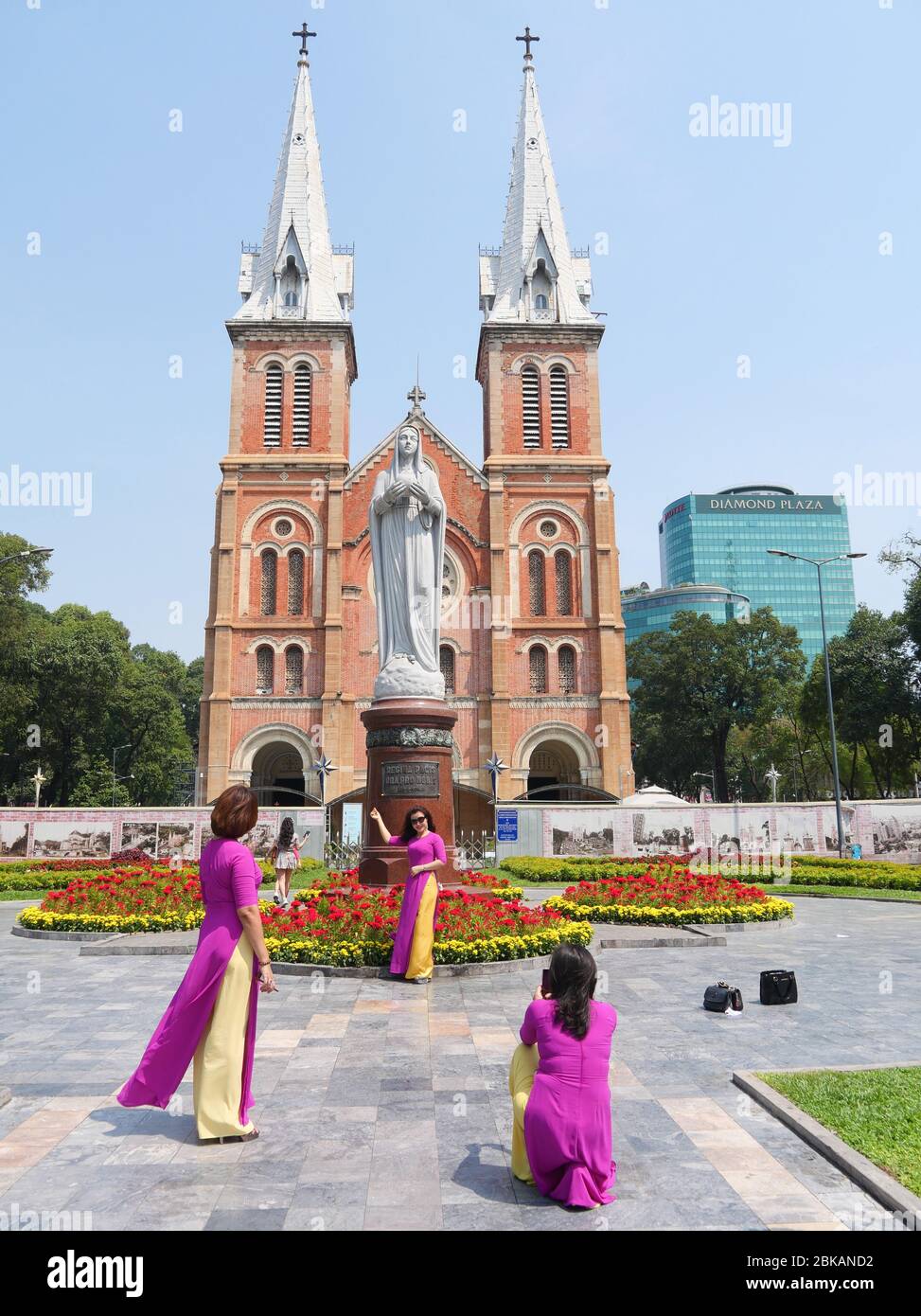 Ho Chi Minh City, Vietnam - 30 aprile 2020: Tre Signore in magenta brillante tradizionale vietnamita lungo vestito di fronte alla Cattedrale di Notre-Dame Basi Foto Stock