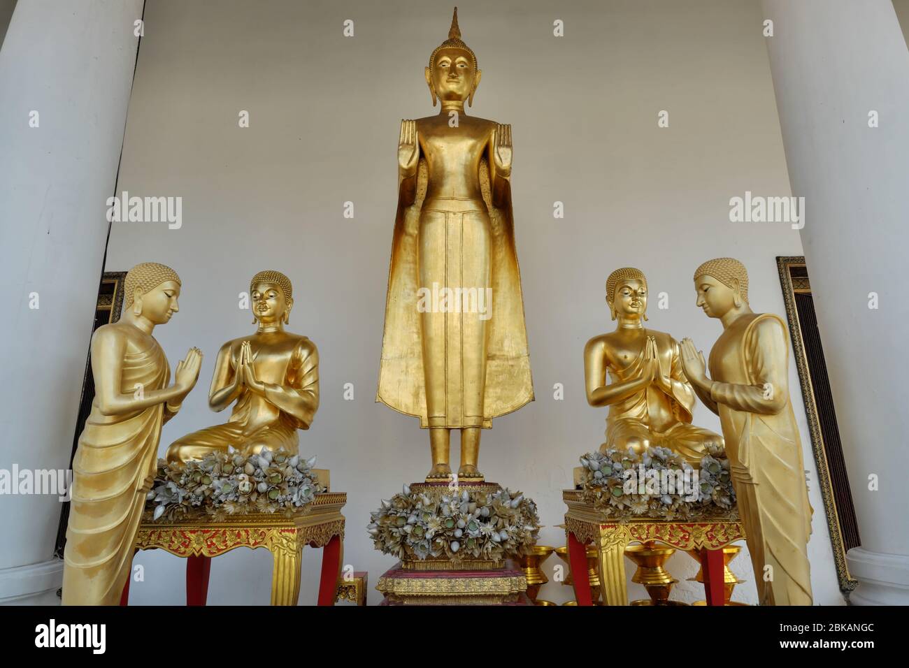 Una statua di Buddha raffigurante il Buddha nell'Abhaya Mudra, cioè un gesto di paura disperdente, fiancheggiata da figure di monaci; Wat Ratchanadta, Bangkok, Thailandia Foto Stock