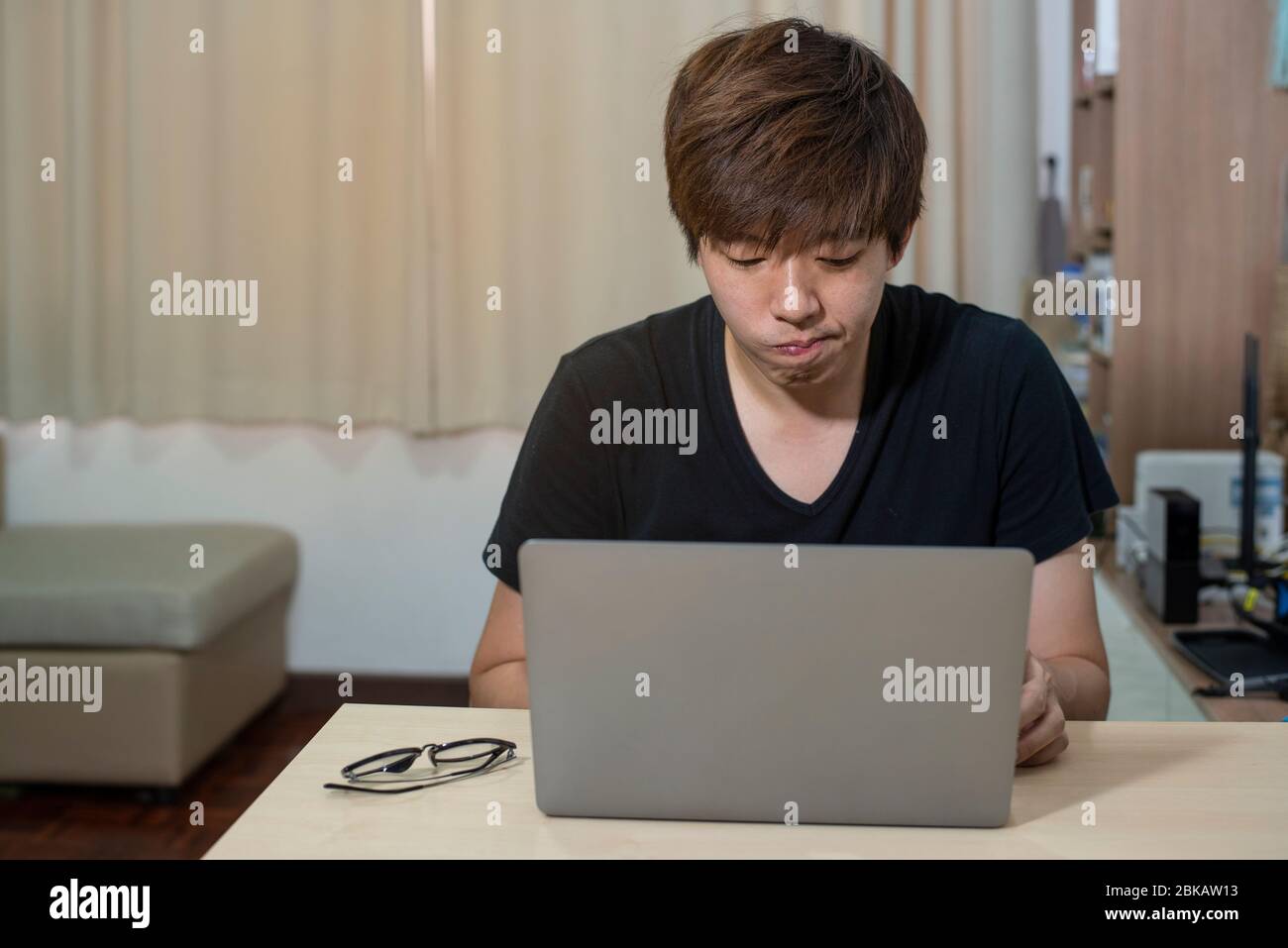 L'uomo ufficiale asiatico lavora da casa. L'uomo lavora in azione a casa. Uomo con notebook che lavora in remoto tramite connessione internet ad alta velocità. Tecnologia di comunicazione Foto Stock