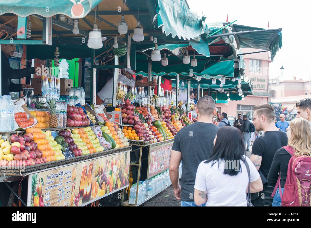 I turisti passeggiando accanto al negozio di succhi di frutta nella piazza del mercato della medina di Marrakesh, aka Djemaa el fna, Marrakech, Marocco Foto Stock