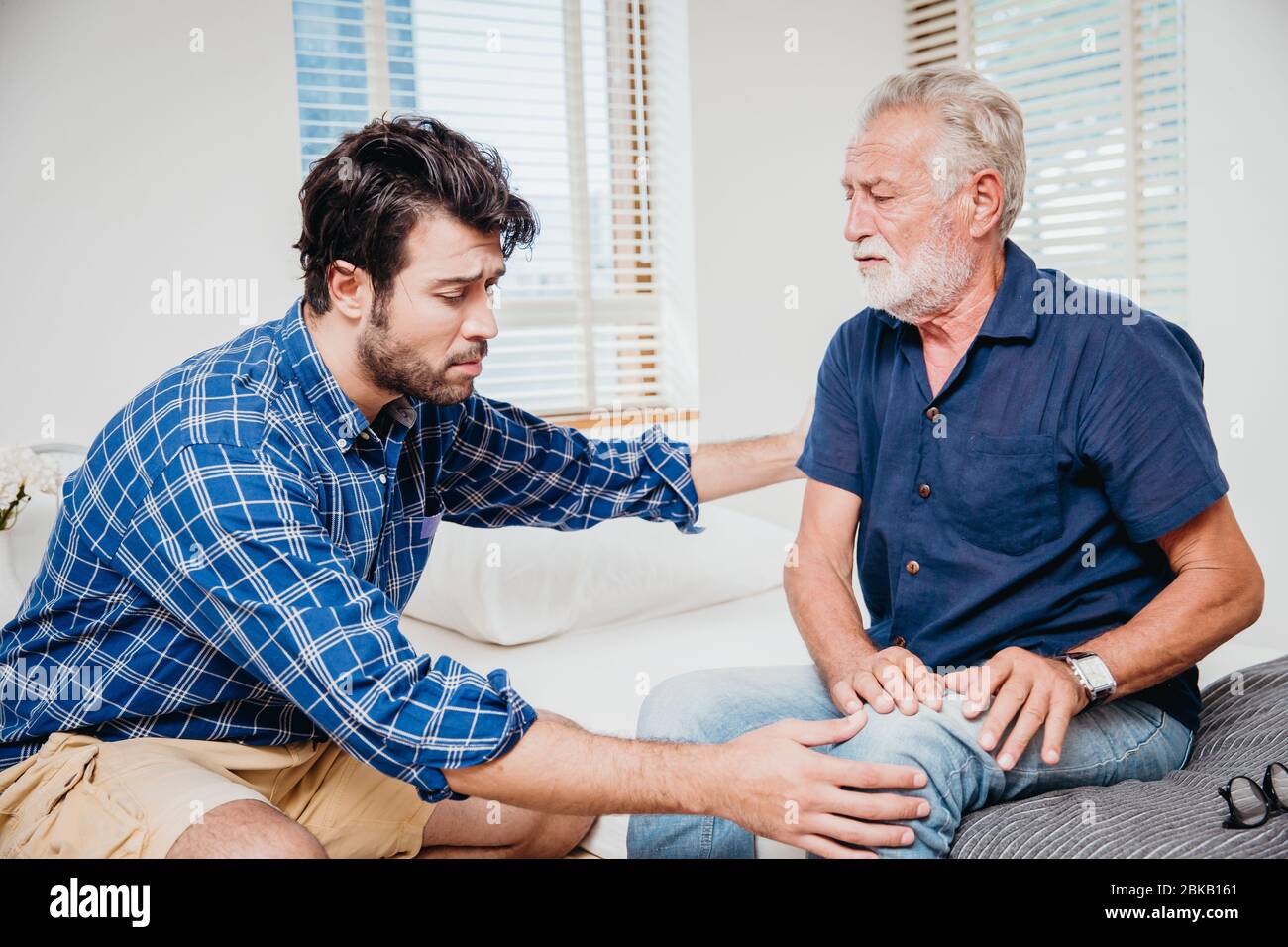 Giovani uomini salute anziani zio in casa, vecchio dolore alle gambe del ginocchio. Foto Stock