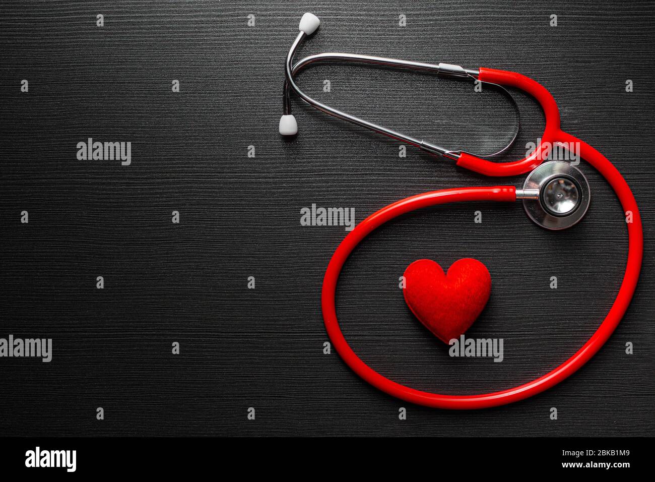 Stetoscopio medico con cuore rosso su sfondo nero tavolo in legno con spazio per testo. Foto Stock