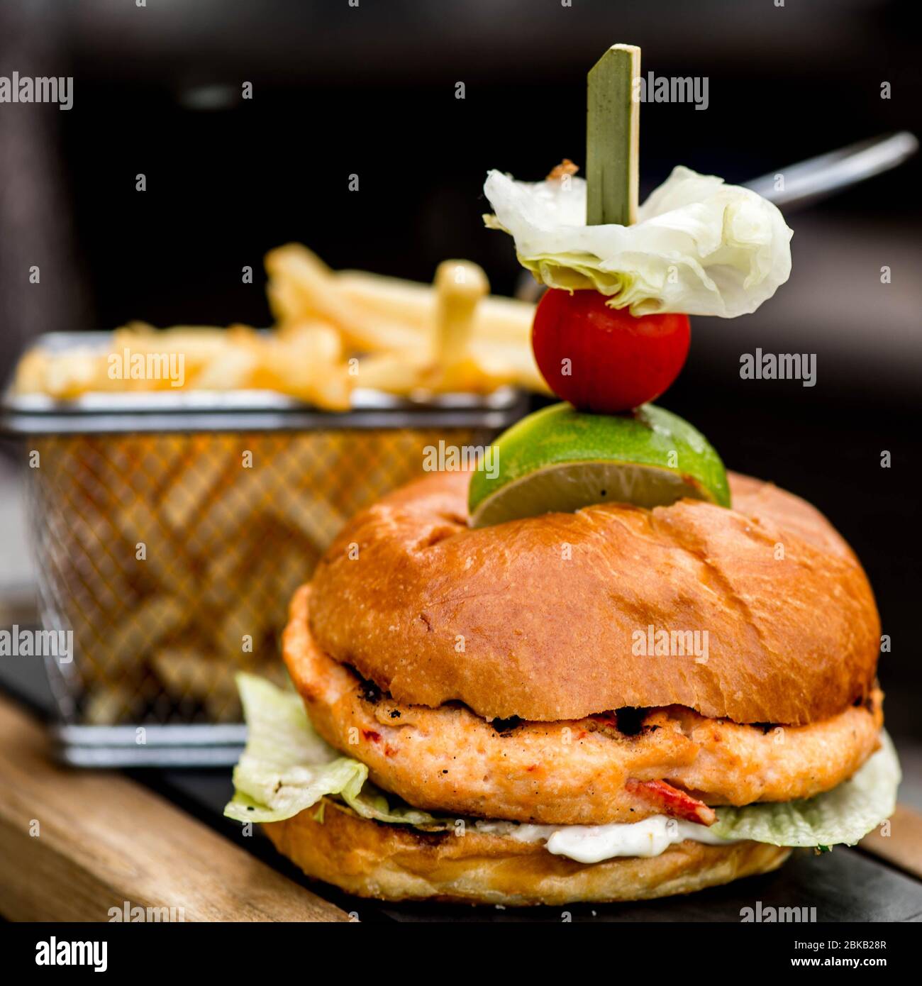 Hamburger di pollo piccante appena cucinato in una panca tostata con un cestino di patatine o di fritte, senza persone Foto Stock