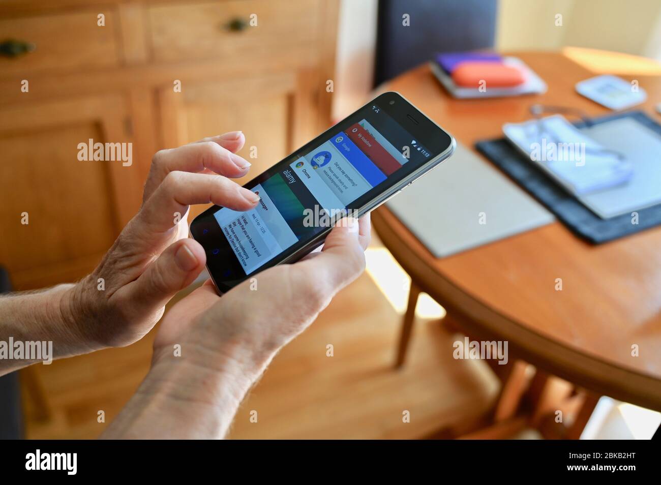 Una donna anziana accede a Internet dal suo telefono cellulare a casa. Foto Stock