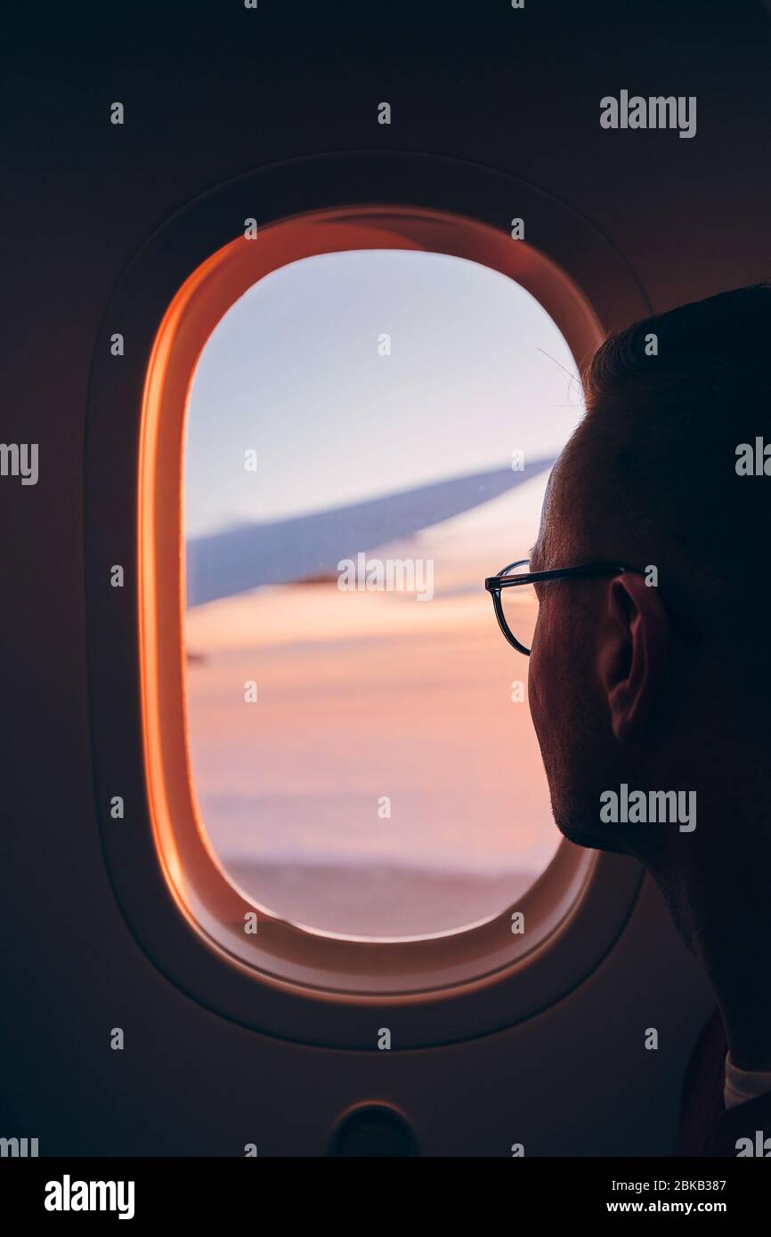 Uomo che guarda attraverso la finestra di aereo durante il volo sopra le nuvole al tramonto. Foto Stock