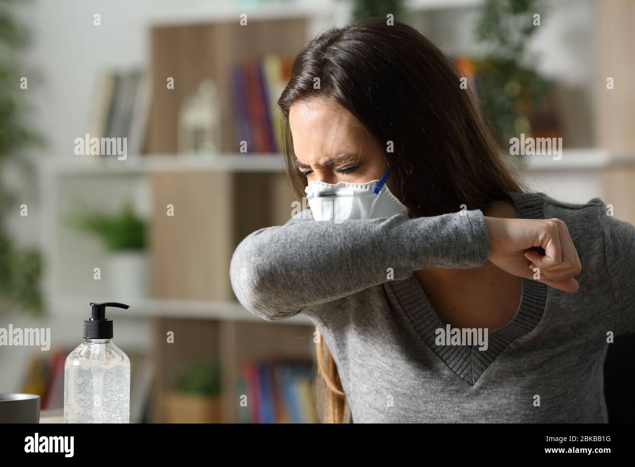 Donna malata con maschera tosse sul gomito a causa di infezione da coronavirus a casa durante la notte Foto Stock