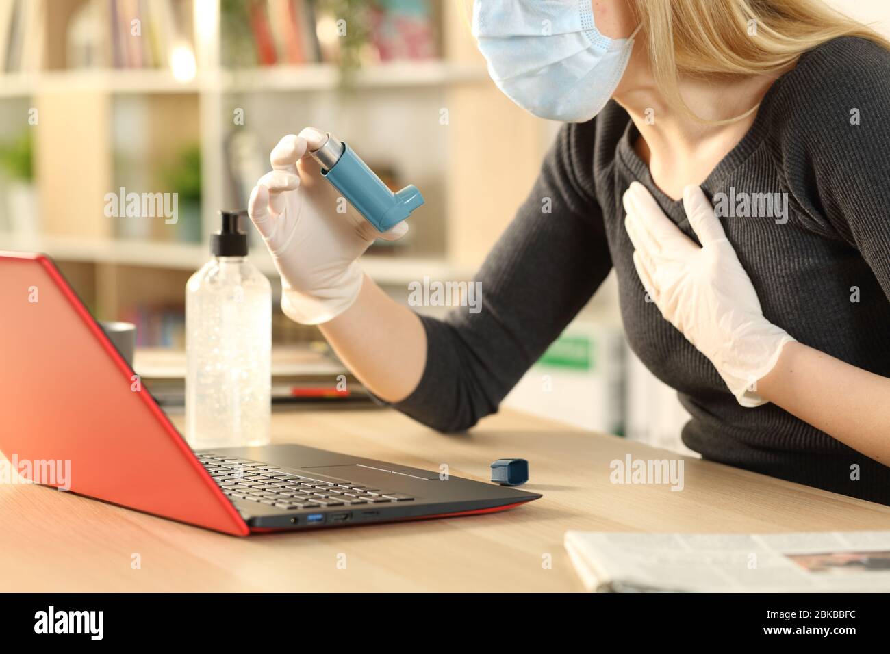 Donna asmatica che tiene l'inalatore soffocante con i sintomi del coronavirus seduto su una scrivania a casa Foto Stock