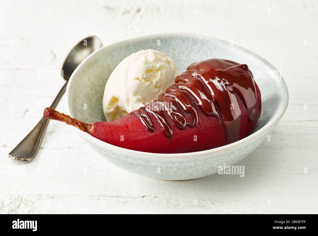 Pera in camicia al vino rosso, dessert decorato con gelato e cioccolato fuso Foto Stock