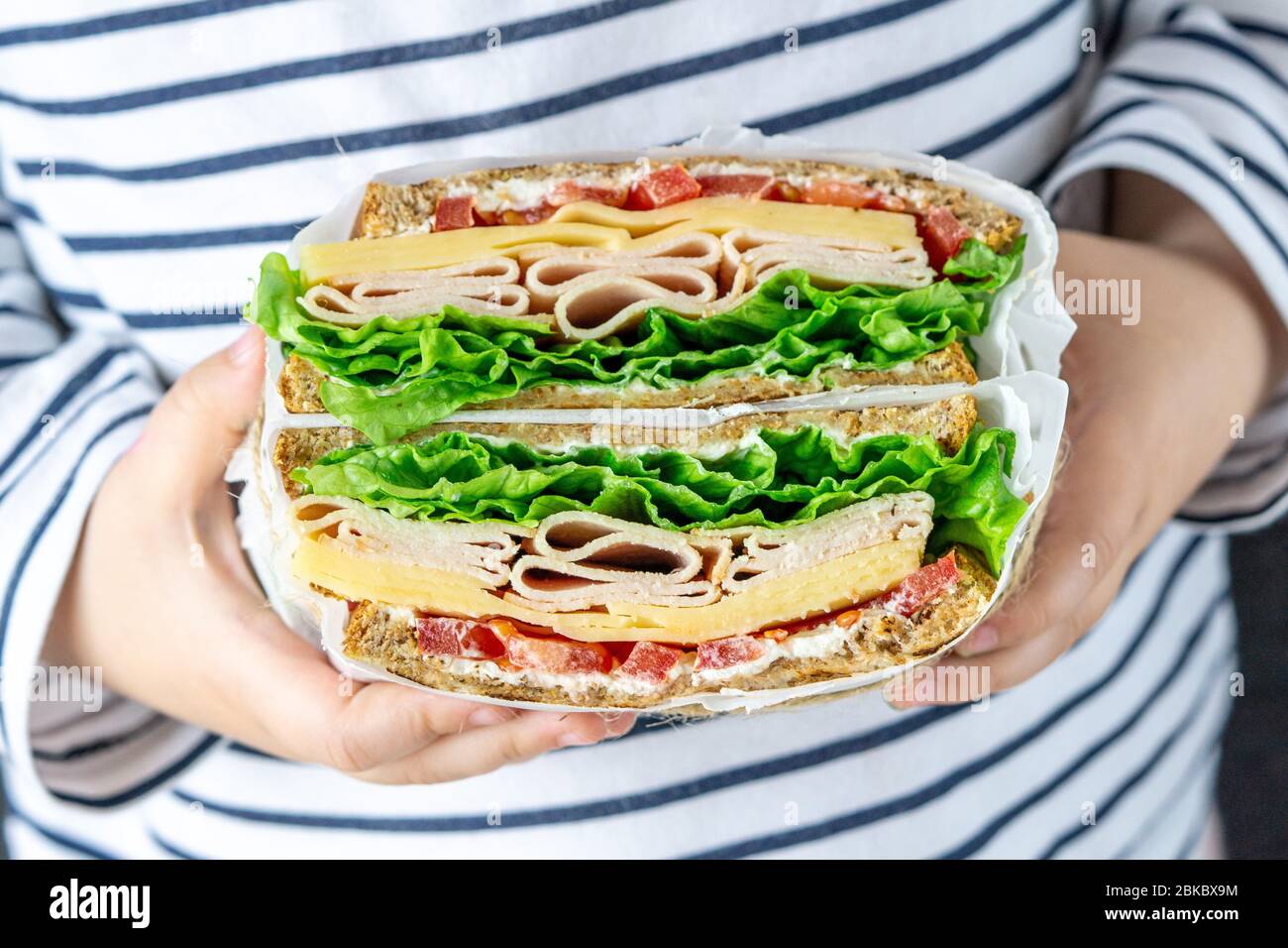 Mani tiene il panino club con prosciutto, lattuga, formaggio, pomodoro. Primo piano. Foto Stock