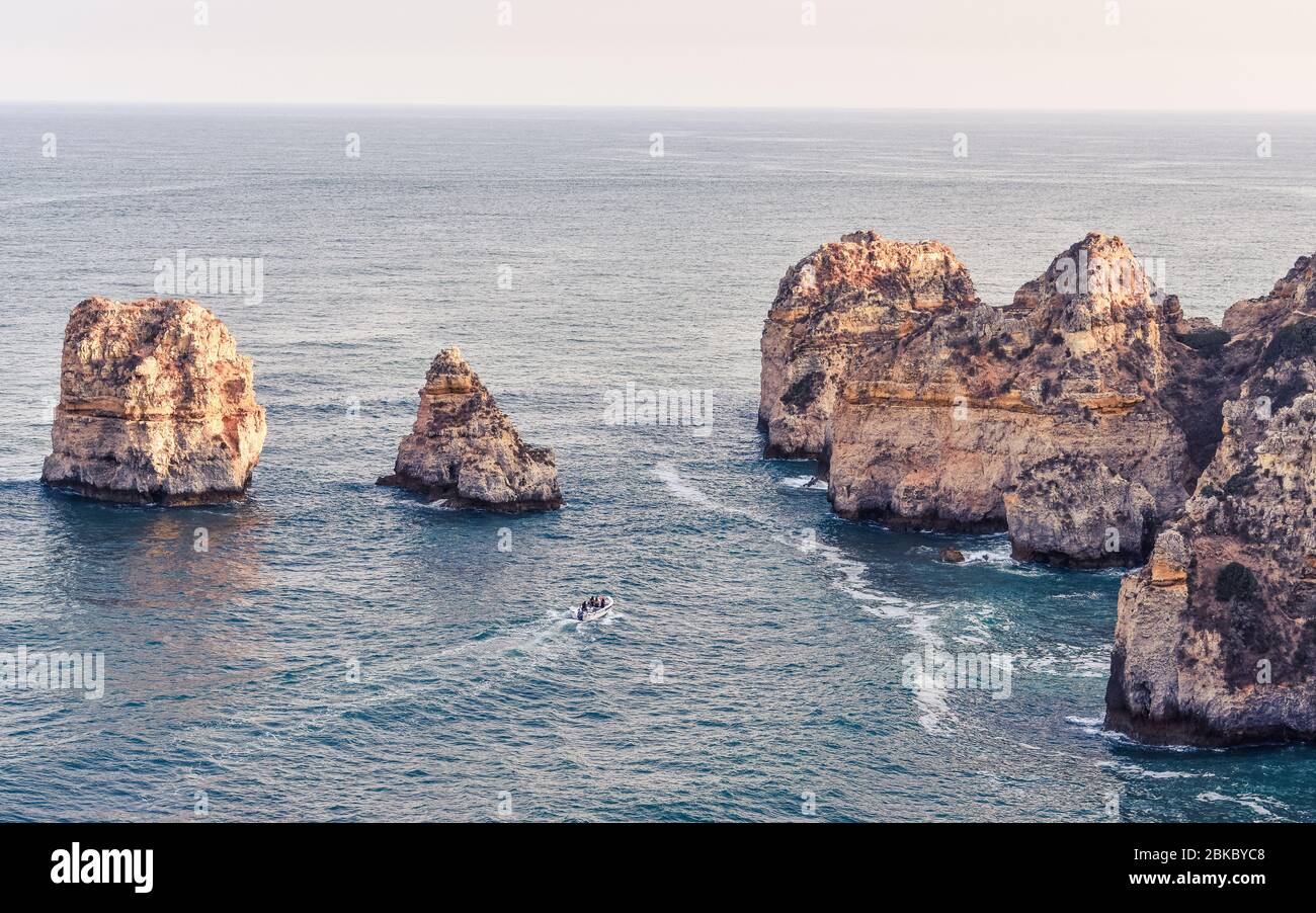 Salando in barca attraverso scogliere di rocce di colore arancione e acque di truqeussian. Concetto di turismo e di viaggio. Algarve, Portogallo Foto Stock
