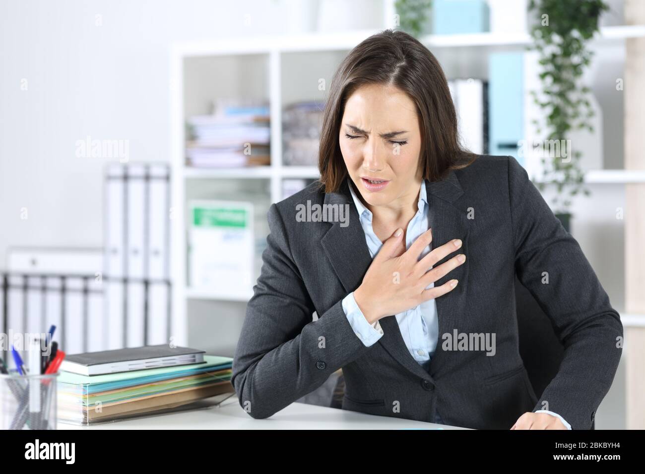 Donna malata dirigente soffocante che tiene il petto seduto su una scrivania in ufficio Foto Stock