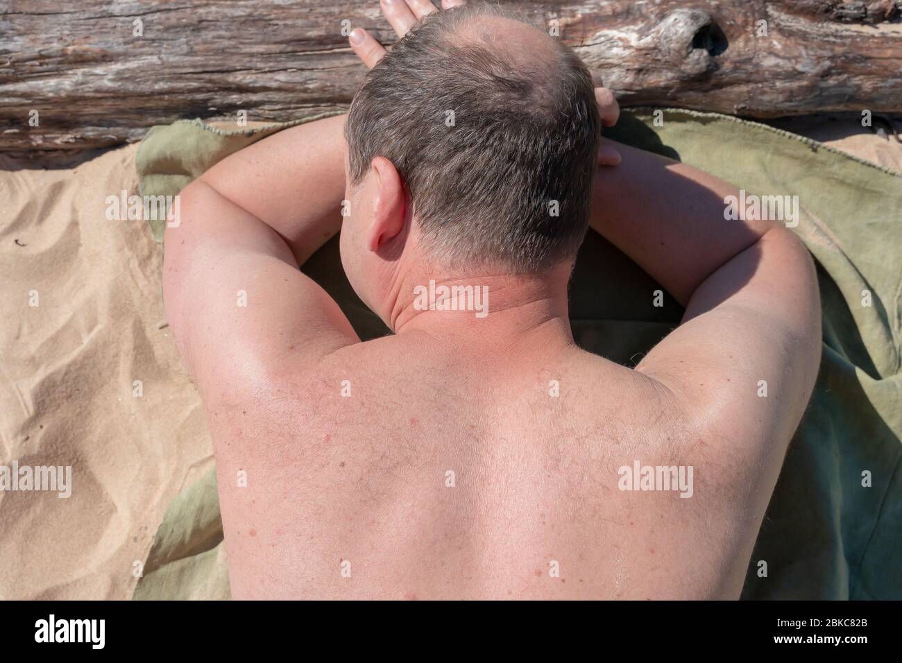 Uomo che prende il sole. Maschio di mezza età che giace sulla spiaggia all'aperto. Il sole splende sul suo corpo. Foto Stock