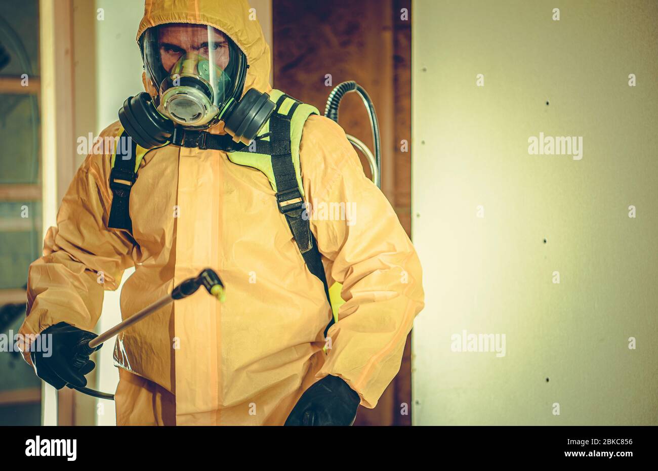 Lavoratore in tuta Hazmat e maschera facciale completa spruzzatura liquido di disinfezione per uccidere batteri e virus all'interno dell'edificio. Foto Stock