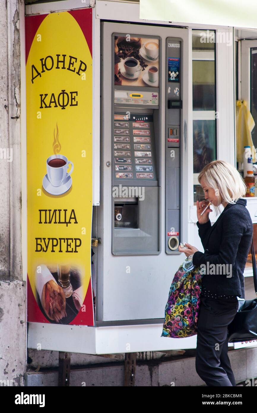 Lady afferra un caffè veloce in movimento da un distributore automatico all'aperto per le strade di Plovdiv, Bulgaria Foto Stock