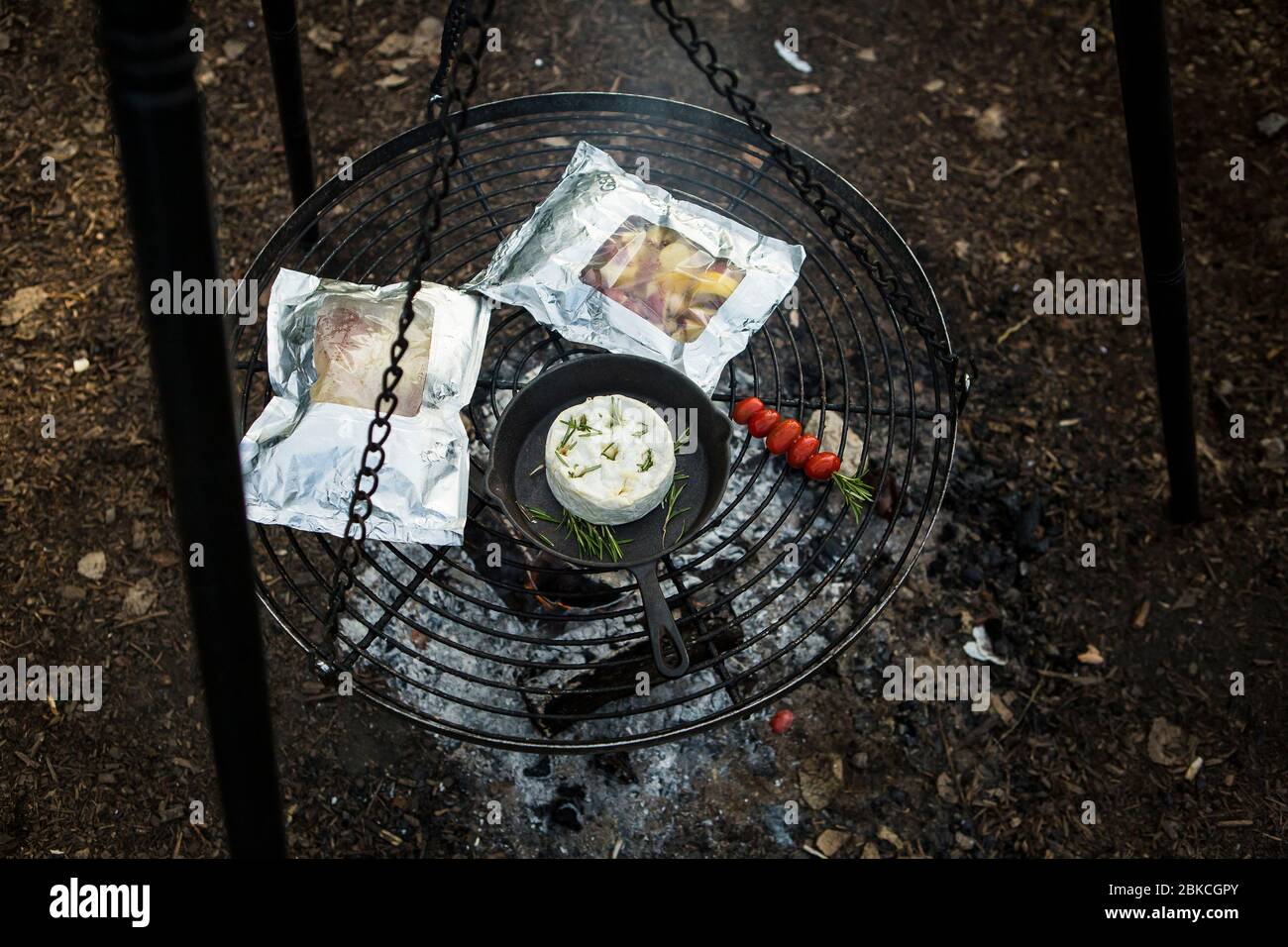 Cucina del cibo su un fuoco su un barbecue appeso a Wowo's, un campeggio familiare in Sussex Foto Stock