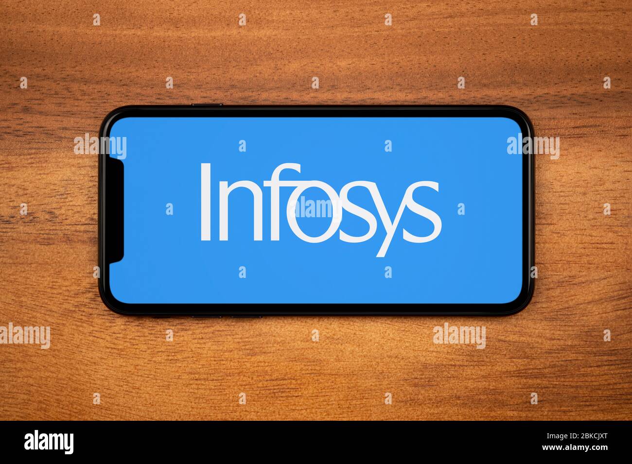 Uno smartphone con il logo Infosys si appoggia su un tavolo di legno (solo per uso editoriale). Foto Stock