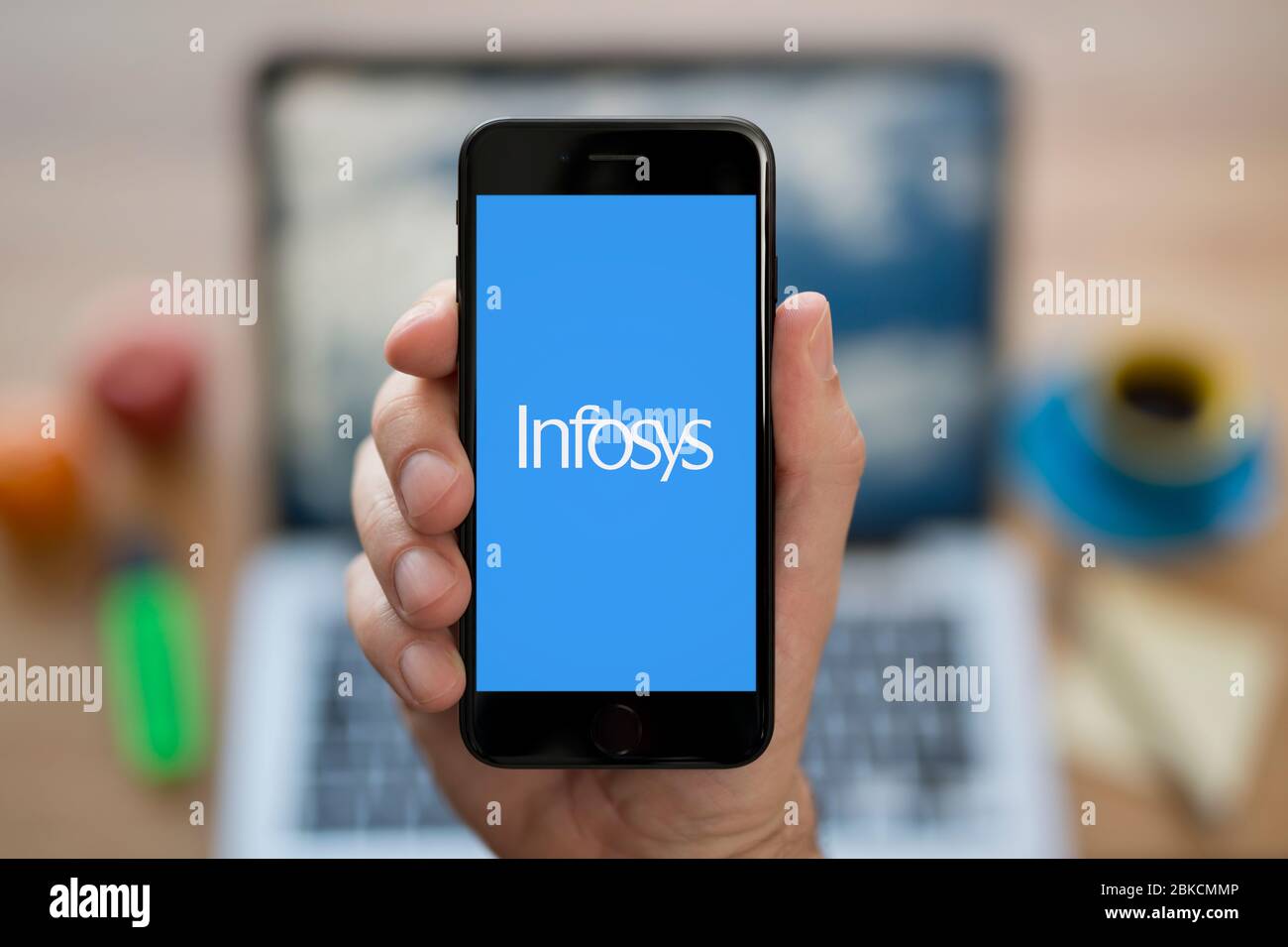 Un uomo guarda il suo iPhone che mostra il logo Infosys (solo per uso editoriale). Foto Stock