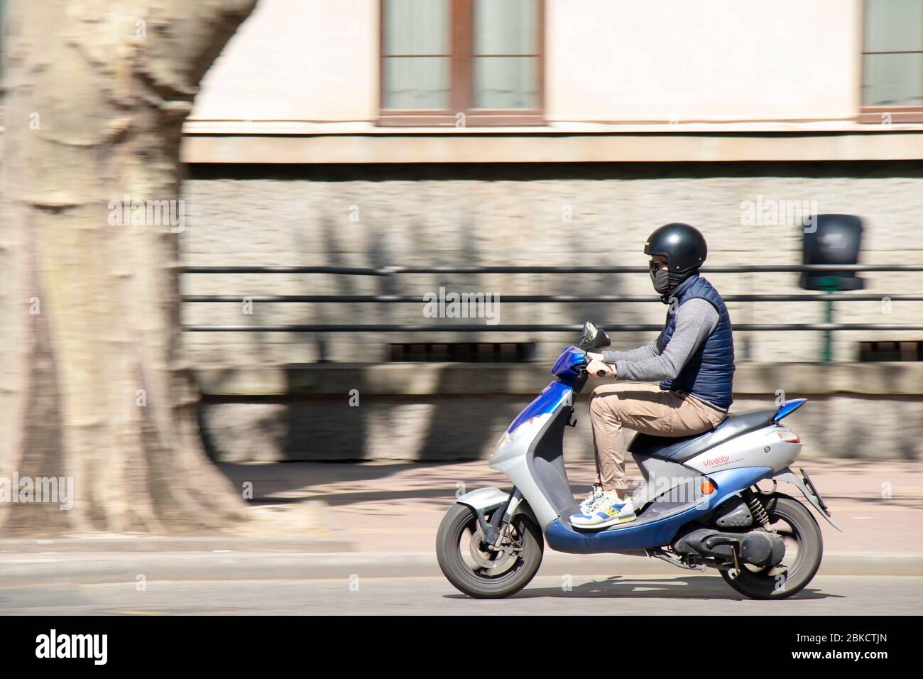 Belgrado, Serbia - 23 aprile 2020: Un giovane uomo che indossa casco, maschera facciale e occhiali da sole a bordo di una moto scooter in città Foto Stock