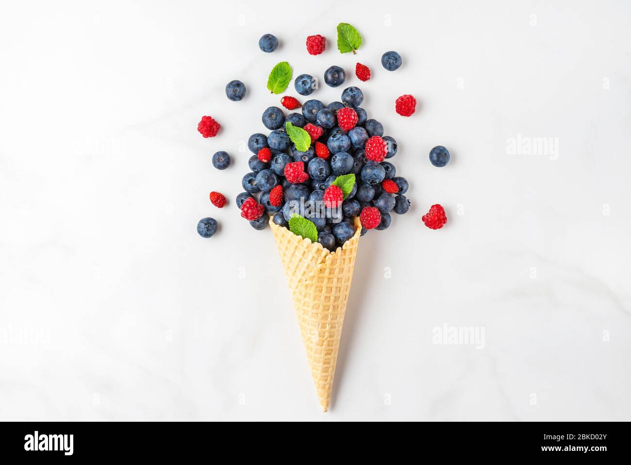 Mirtilli e lamponi estivi freschi con menta in cono di waffle su sfondo in marmo bianco. Concetto di cibo estivo. Piano. Vista superiore con spazio per copia. Foto Stock