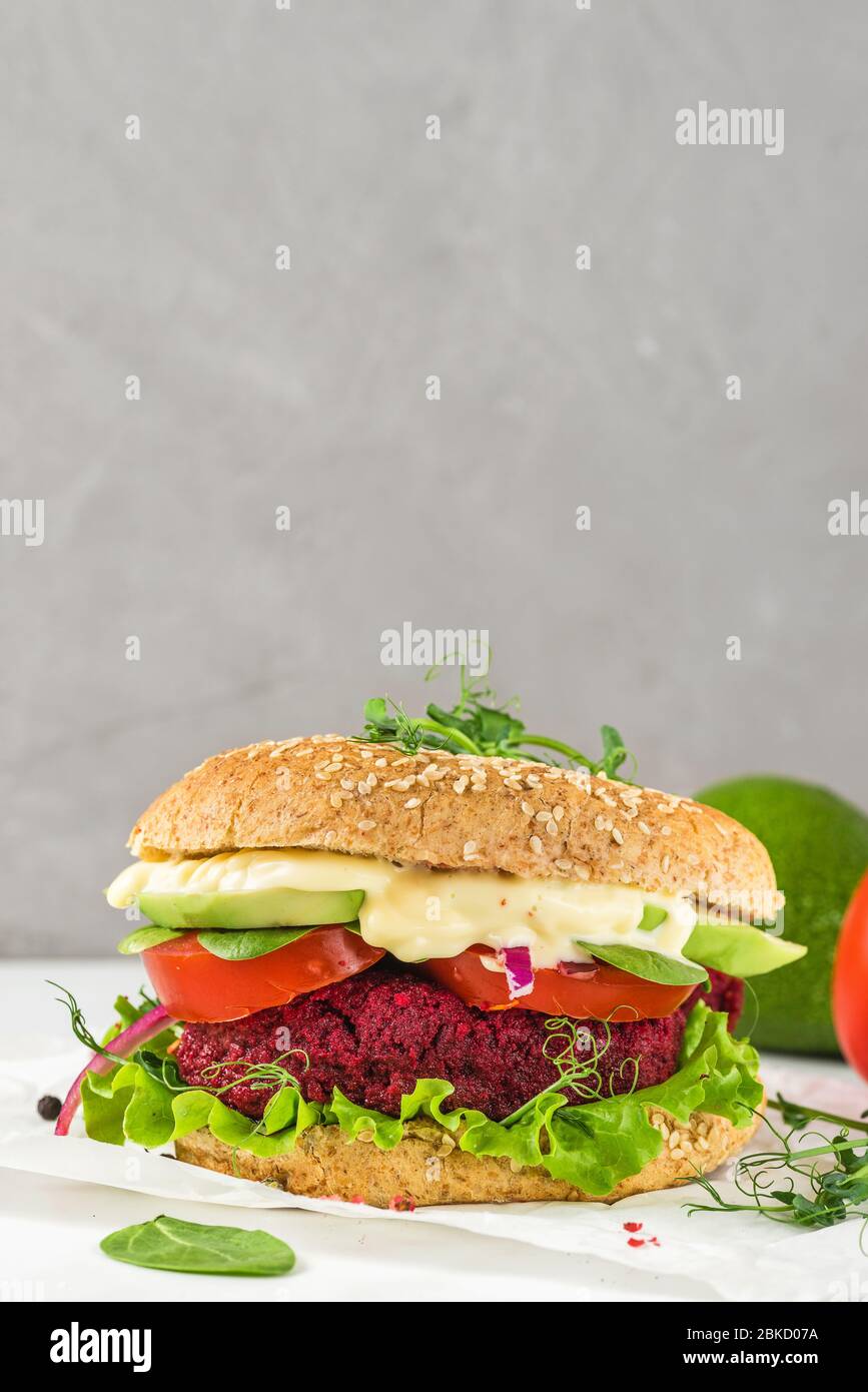 Hamburger di barbabietola vegana con avocado, insalata, pomodoro, germogli e maionese vegana su tavolo in marmo bianco. Orientamento verticale. Fast food sano Foto Stock