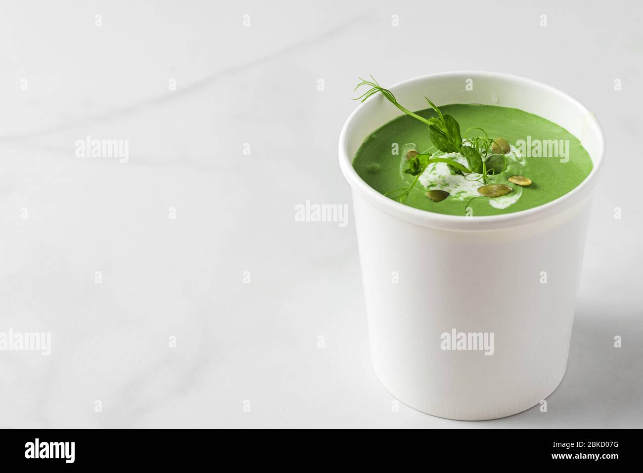 Zuppa di crema verde in confezione di carta o tazza monouso con piselli e spirulina. Concetto di consegna degli alimenti vegani. Mock up Foto Stock