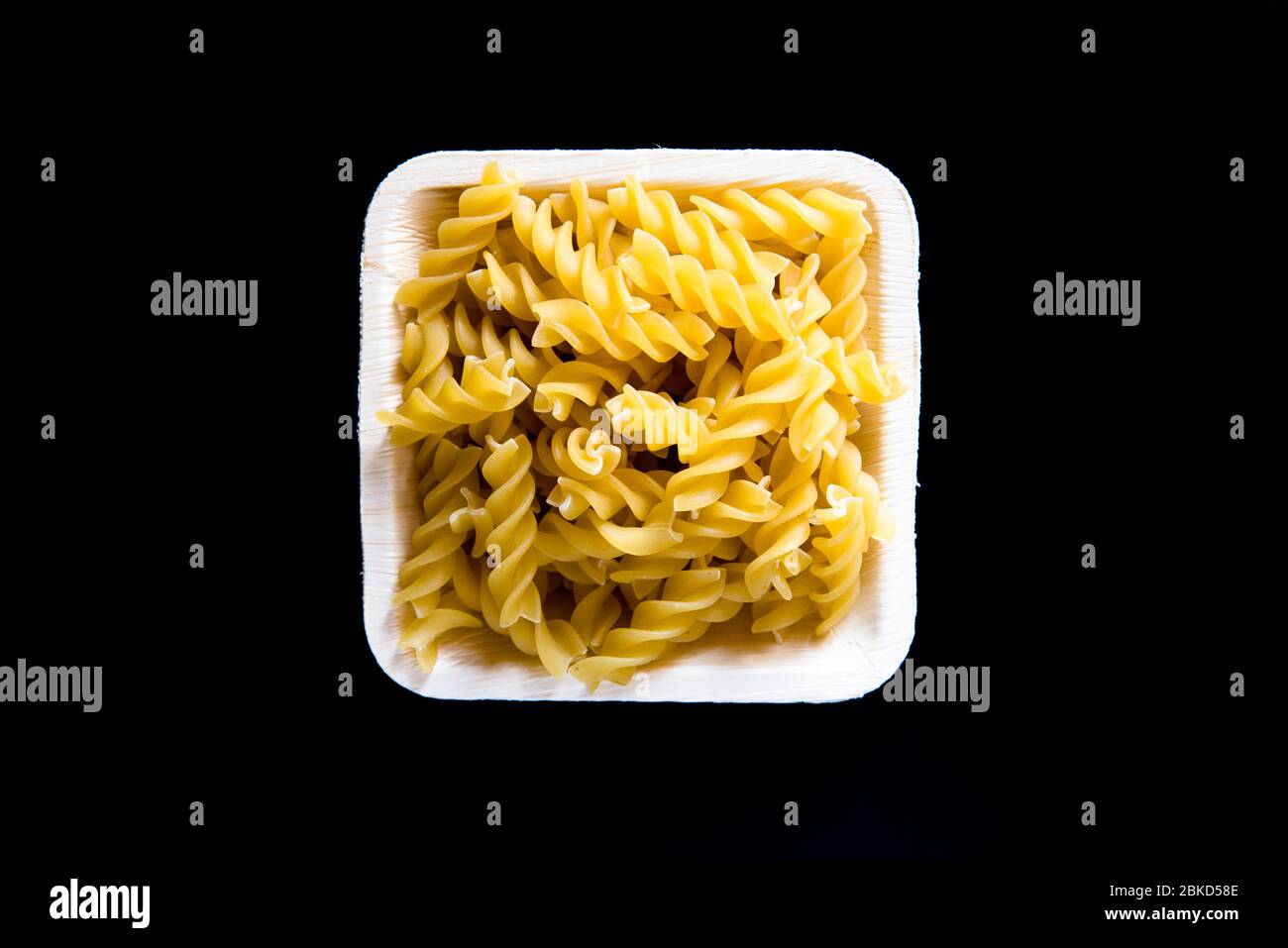 Pasta Fusili cruda in una ciotola su fondo nero Foto Stock